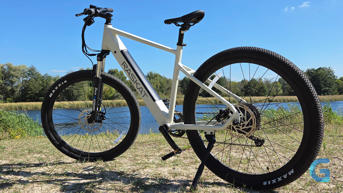 Белый электровелосипед RASKAT E-MTB на грунтовой площадке у воды