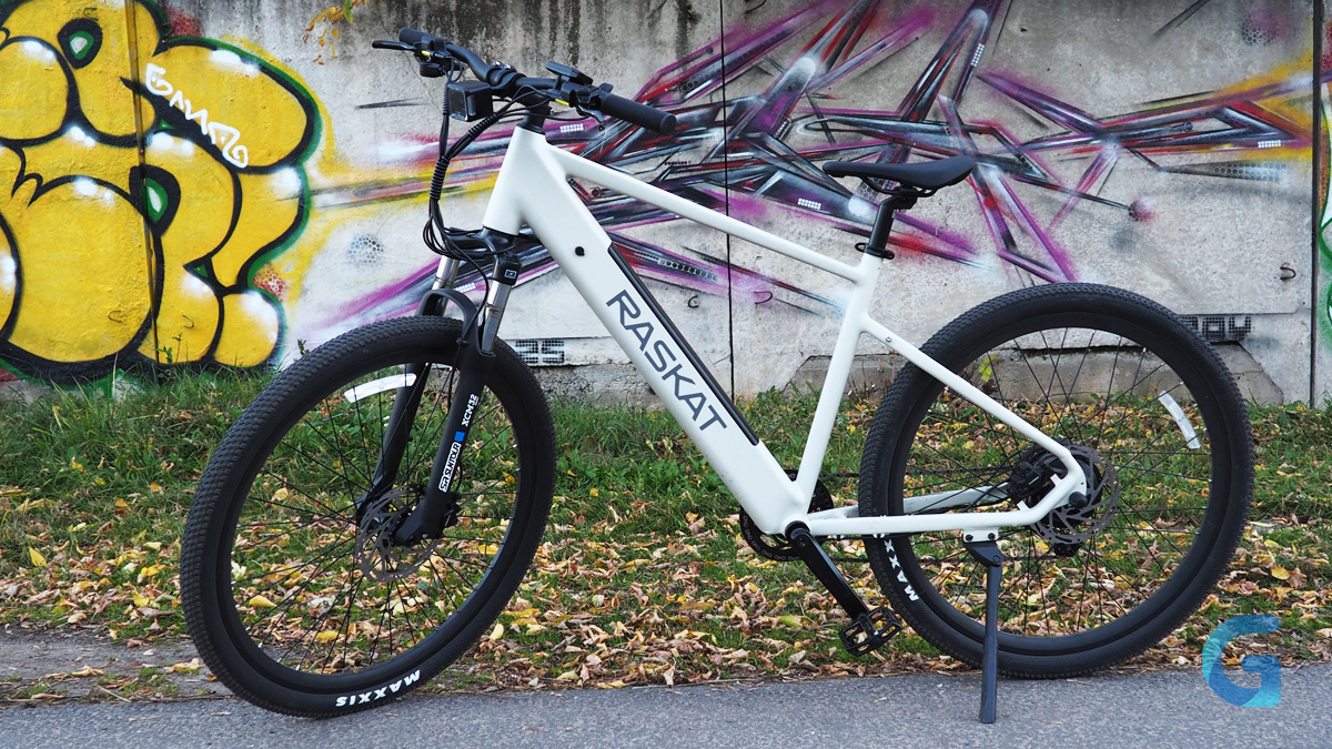 Белый RASKAT E-MTB на подножке у стены с граффити